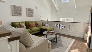 Amplia sala de estar con techo alto, sofá seccional verde, sillón color beige, una mesa de centro y un gran ventanal que proporciona luz natural.