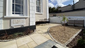 Un edificio con amplias ventanas arqueadas, un patio con un banco y una pequeña jardinera con plantas.
