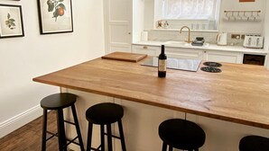 Una cocina con una isla de madera, taburetes de bar, una botella de vino y un ventanal con vistas a árboles.