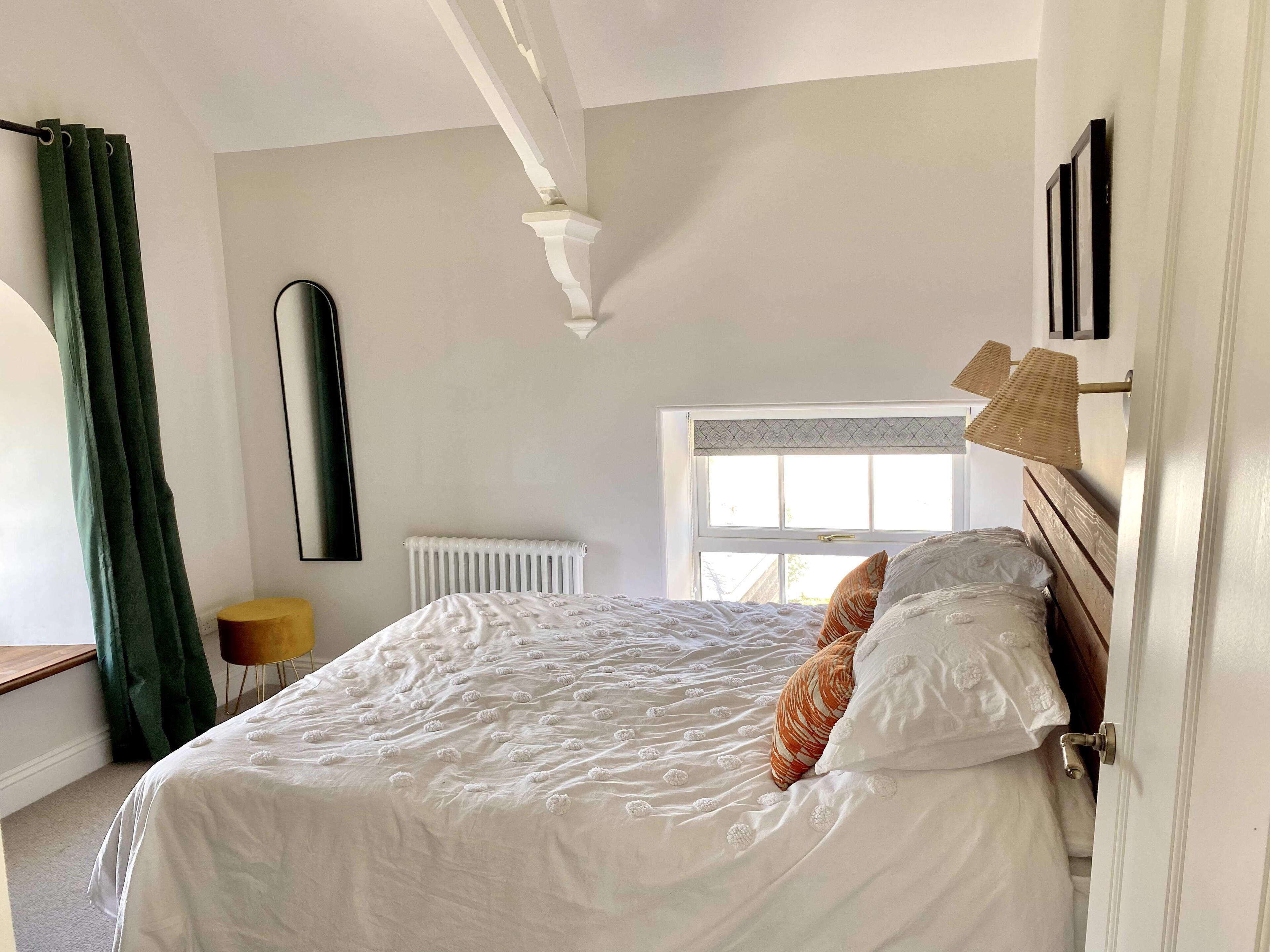 A bedroom with a large bed, a radiator, a window, and a door.