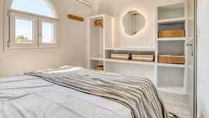 Un dormitorio con cama, estanterías empotradas con cestas, un espejo redondo y una ventana con vistas.