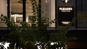 Hotel moderno urbano com uma grande placa iluminada exibindo o nome 'PLEIADES' e o endereço 'DIEKOSINIS 21, 1º andar'.