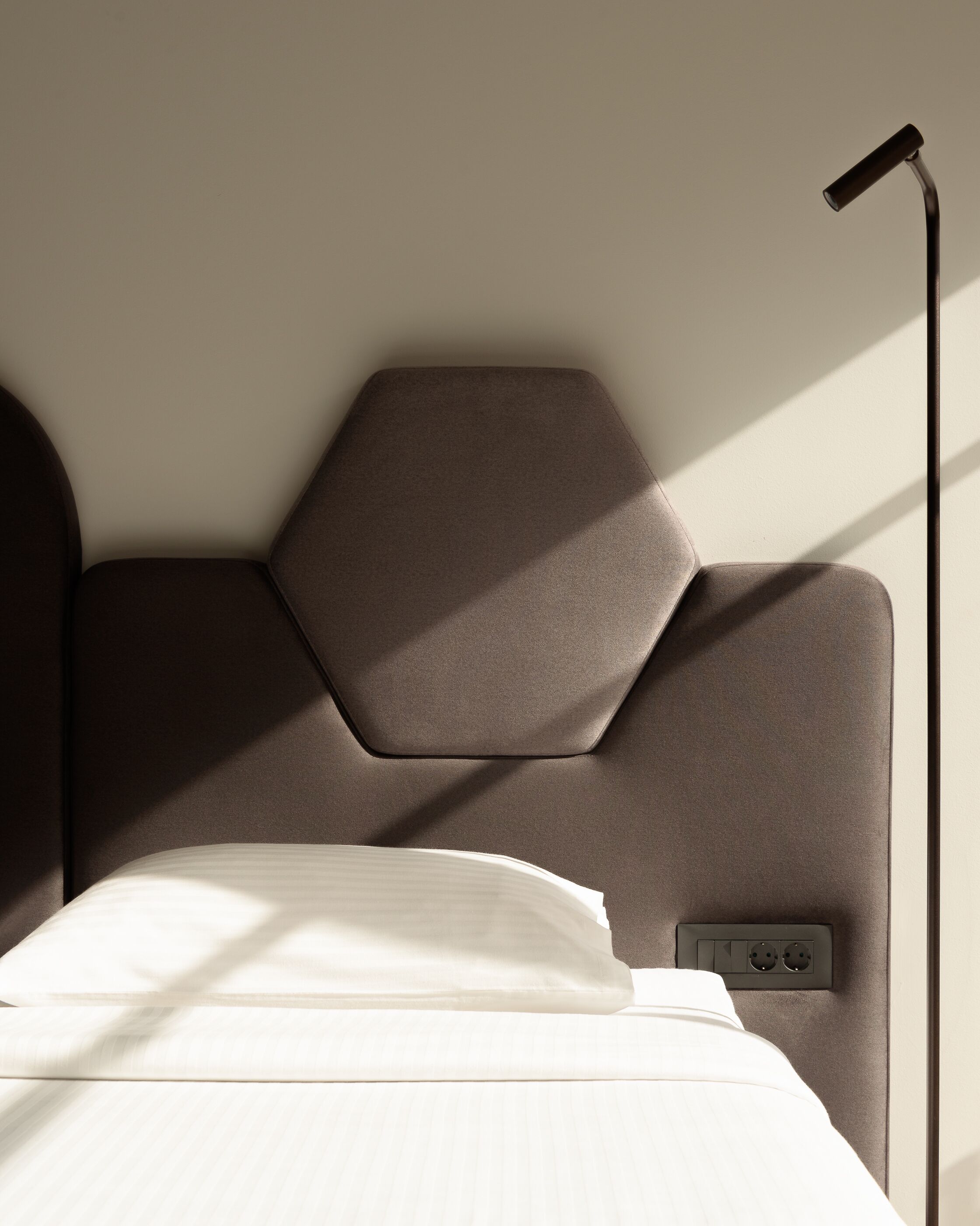 Un letto moderno con testiera geometrica, un comodino e una lampada da lettura fissata al muro.