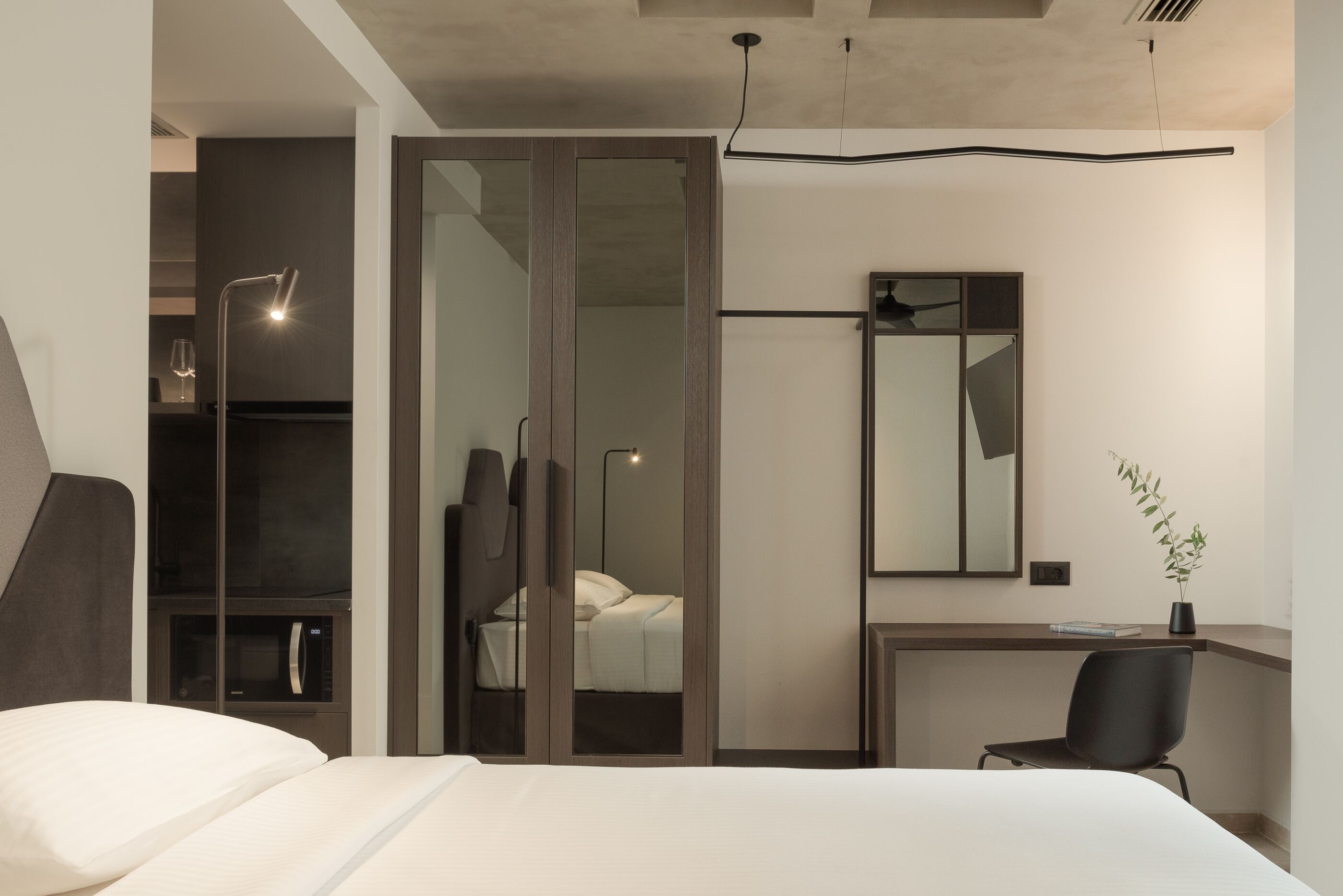 Un dormitorio moderno con cama, escritorio, silla, espejo y planta.
