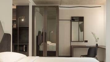 A modern bedroom with a bed, a desk, a chair, a mirror, and a plant.