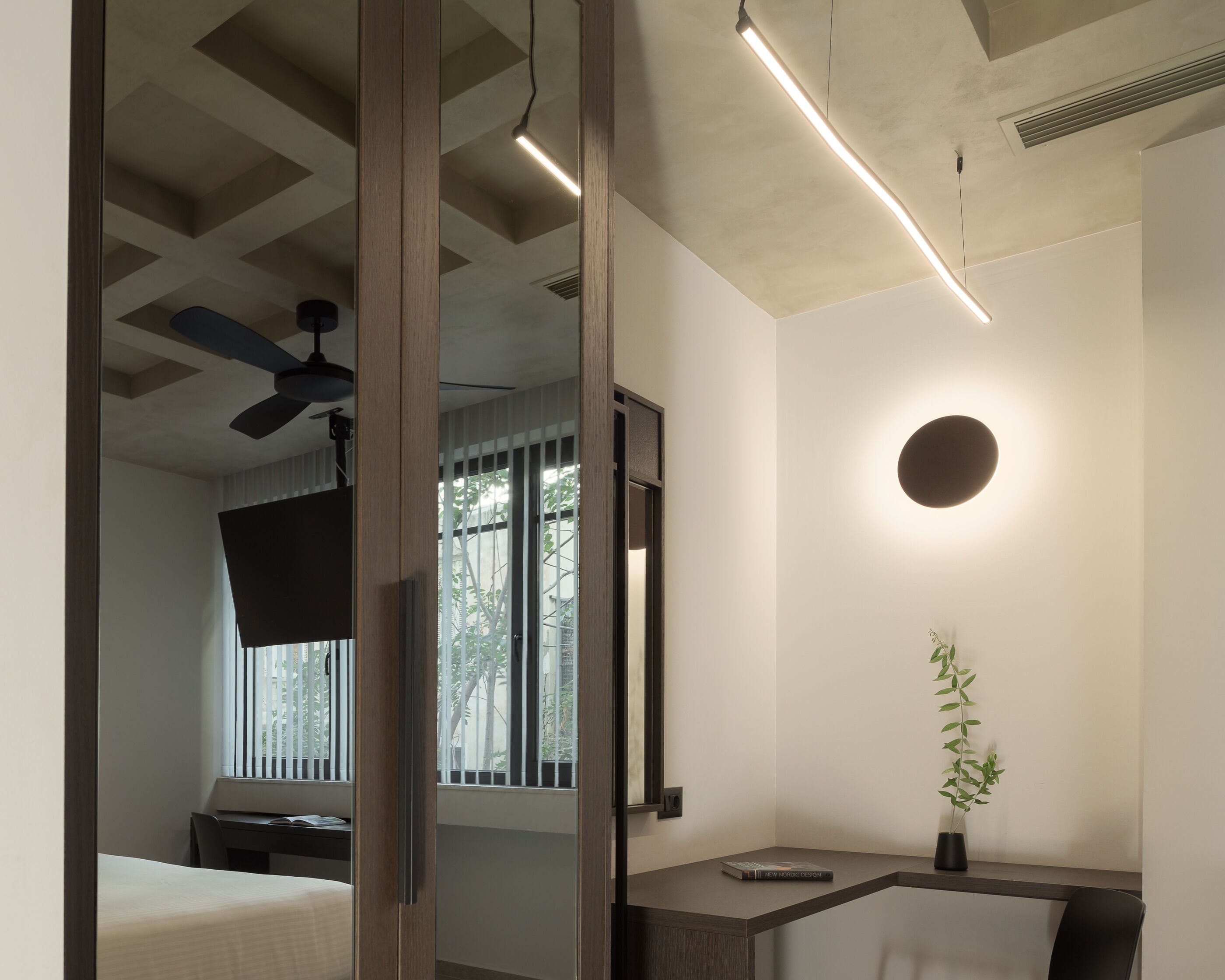 Un dormitorio moderno con cama, escritorio, silla, ventilador de techo, ventana con persianas y mesita de noche con planta.