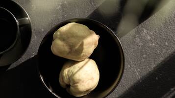 A bowl containing two dumplings on a dark surface with shadows.