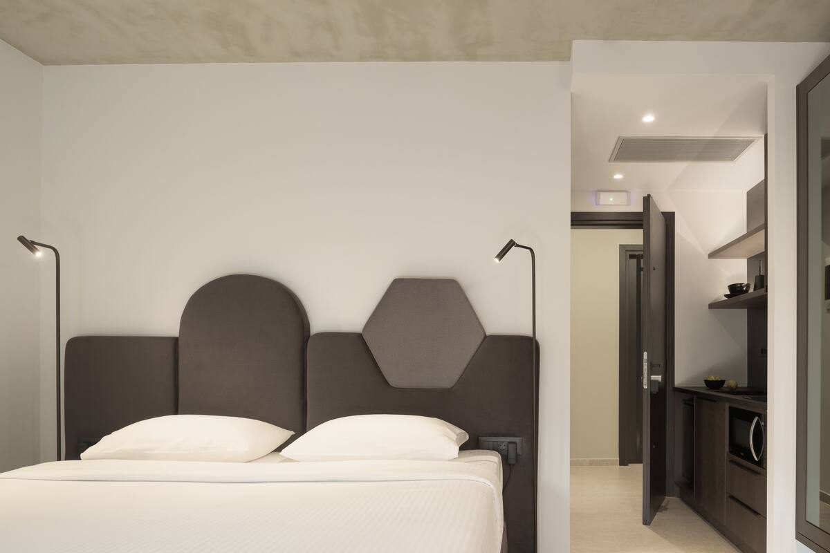 A modern bedroom with a large bed, a headboard with geometric shapes, and a bedside table with a lamp.