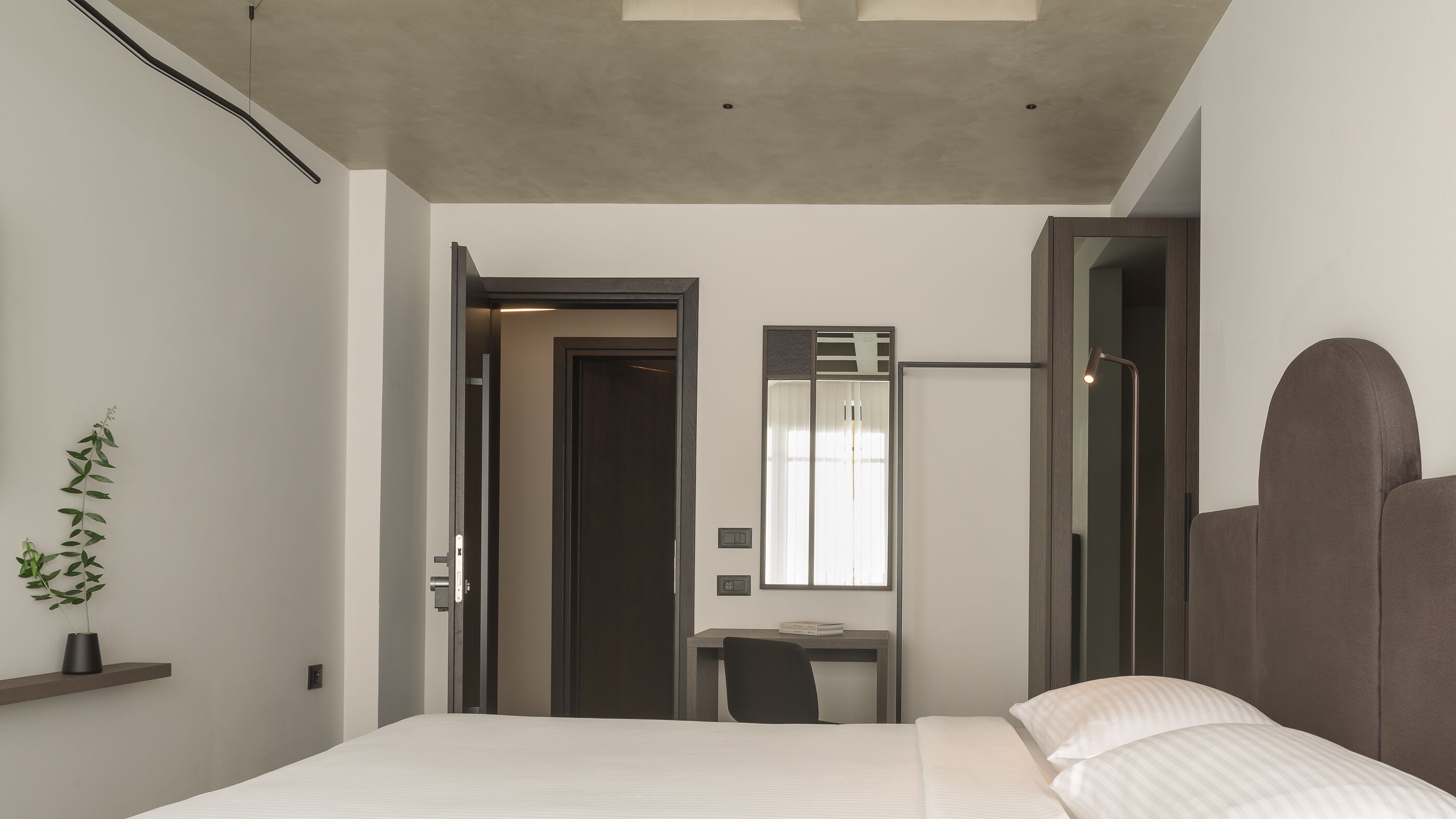 A modern hotel room with a bed, a desk, and a mirror.
