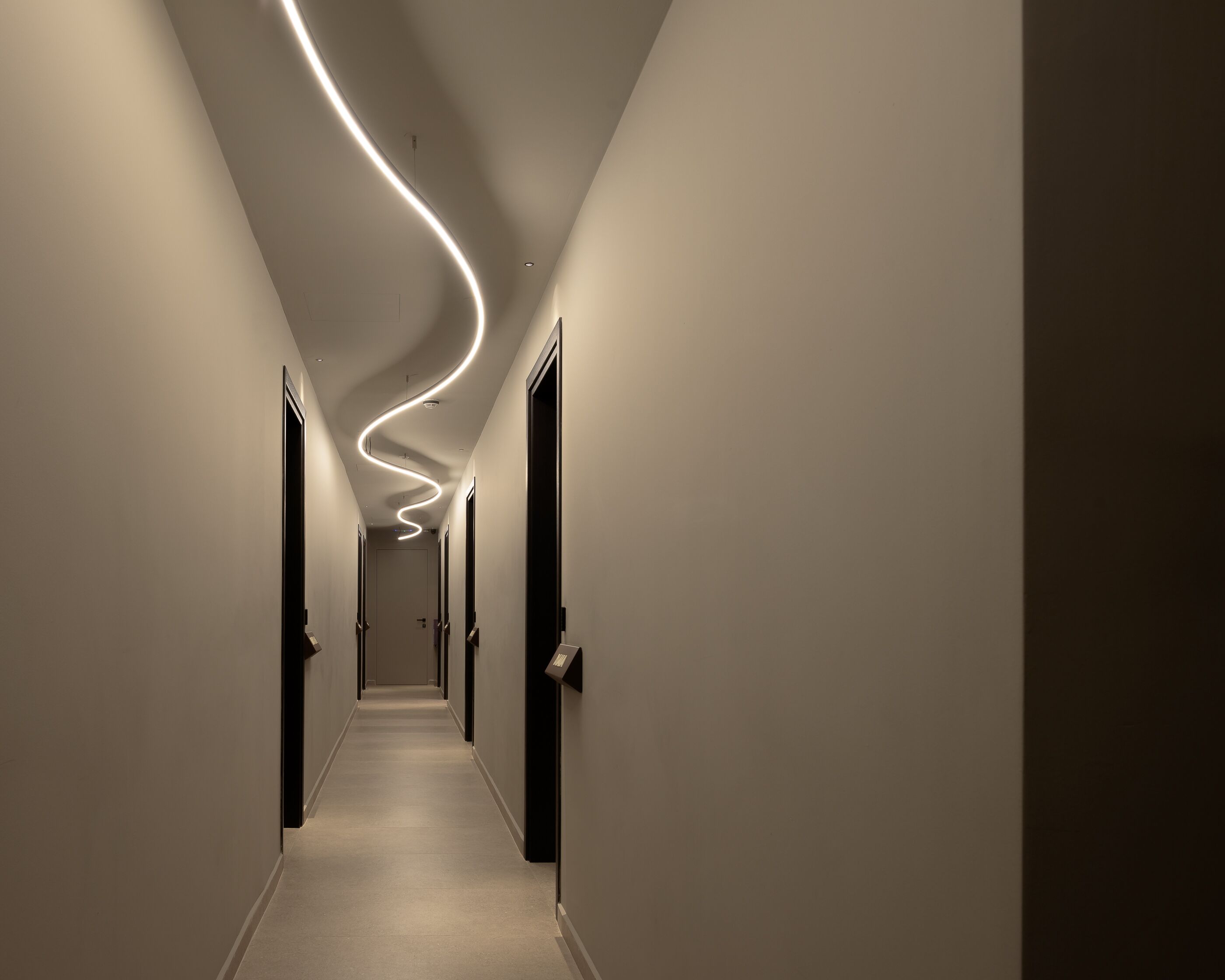 A hallway with a modern light installation curving along the ceiling.