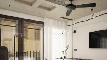 A hotel room with a bed, a desk, a chair, a TV mounted on the wall, a ceiling fan, and a view of the outside through a sliding glass door.