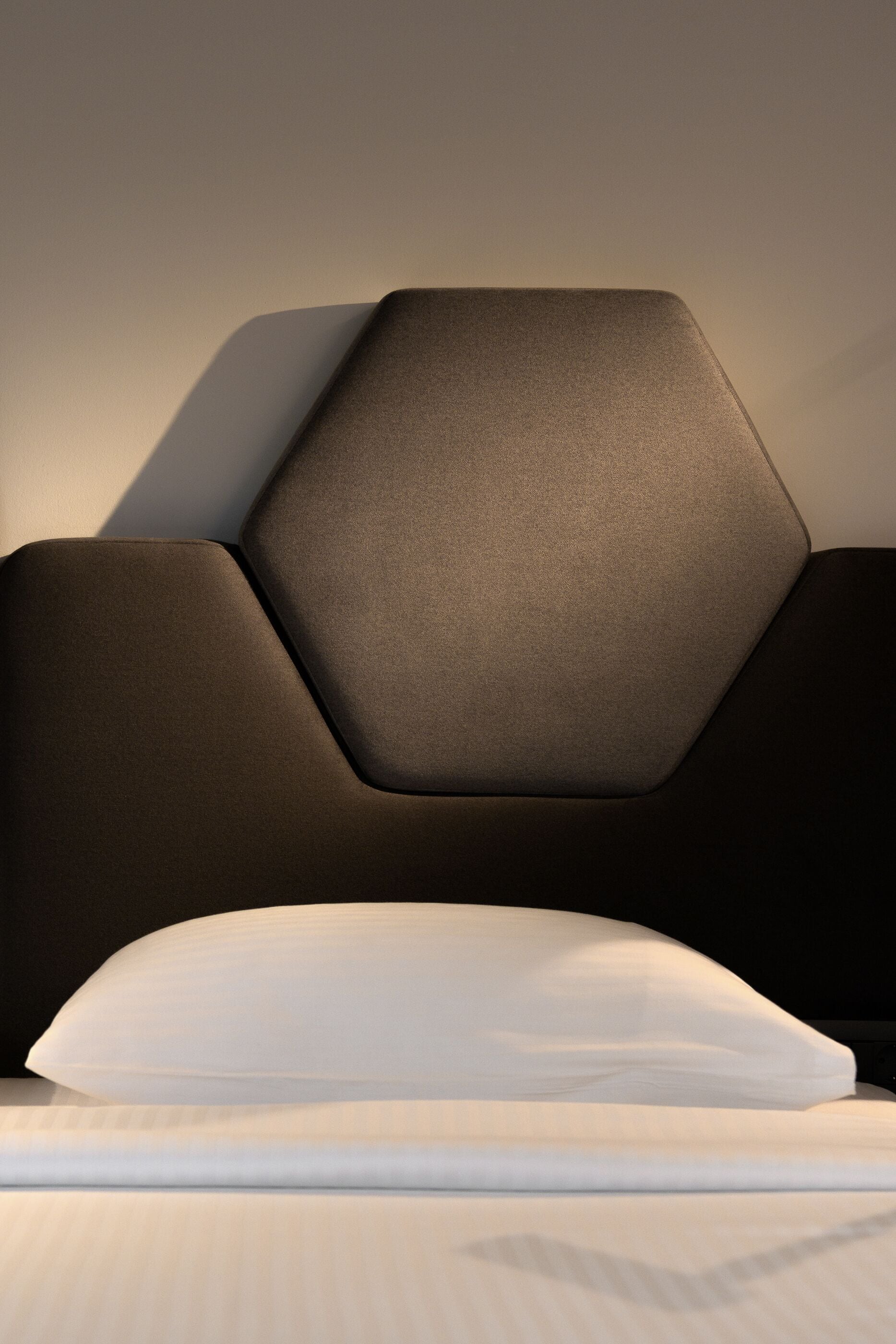 Un lit moderne avec une tête de lit aux motifs géométriques et un drap blanc parfaitement tendu.
