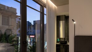Quarto de hotel moderno com amplas janelas, vista da cidade, espelho grande e pia moderna.