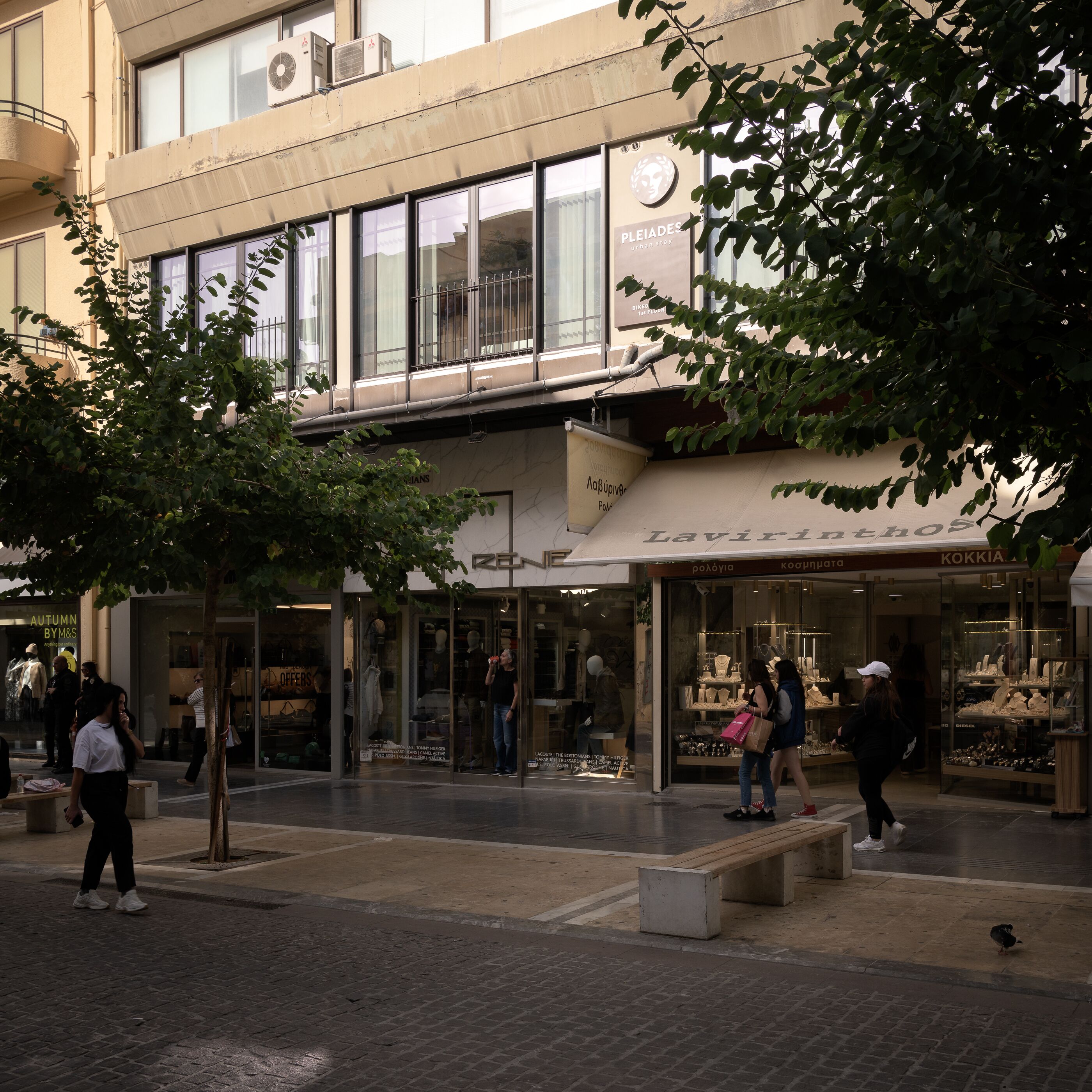 A shopping area with storefronts, benches, and pedestrians.