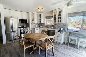 A modern kitchen with white cabinetry, a stainless steel refrigerator, a microwave, and a wooden dining table with chairs.