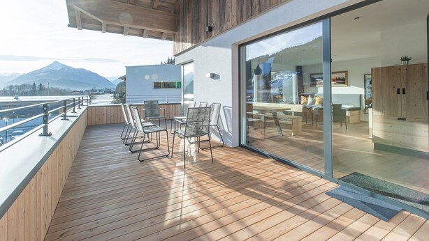 A modern outdoor deck with wooden flooring and metal chairs, overlooking a snowy landscape and mountains. - Apartment Auszeitmit in the Salzburger Sportwelt vacation region (Eben im Pongau)