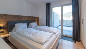 A bedroom with a wooden headboard, two beds, a nightstand, and a large sliding glass door leading to a balcony. - Apartment Auszeitmit in the Salzburger Sportwelt vacation region (Eben im Pongau)