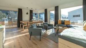 A modern living room with a wooden floor, grey sofas, a dining area with a wooden table, and large windows offering mountain views. - Apartment Auszeitmit in the Salzburger Sportwelt vacation region (Eben im Pongau)