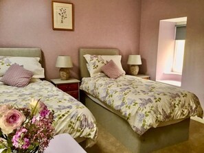Un dormitorio con dos camas, cada una con una mesita de noche y una lámpara. Hay un cuadro enmarcado en la pared y un florero con flores a la izquierda.