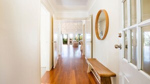 A hallway with a wooden bench, a large mirror, and a door leading to a room with a view of the outdoors. - The Treehouse Vincentia by Latitude South Coast (Vincentia)