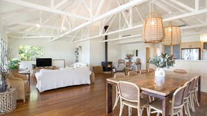 A spacious living area with a large wooden dining table, wicker chairs, a sofa, and a fireplace. - The Treehouse Vincentia by Latitude South Coast (Vincentia)