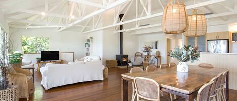 A spacious living area with a large wooden dining table, wicker chairs, a sofa, and a fireplace.