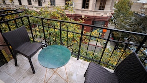 A balcony with two wicker chairs and a small round table, overlooking a cityscape with buildings and trees. - Hotel Verisima (Tbilisi)