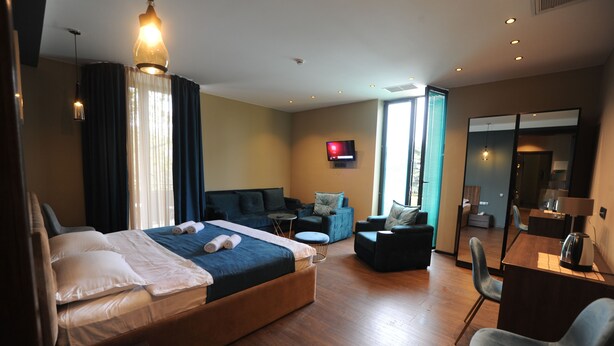 A hotel room with a bed, a sofa, a desk, and a TV. - Hotel Verisima (Tbilisi)