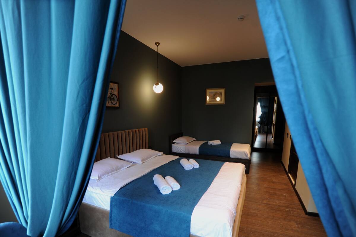 A bedroom with two beds, a ceiling light, and a door leading to another room.
