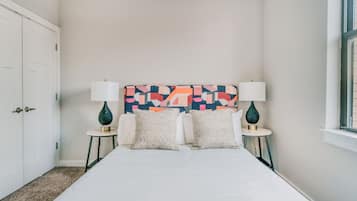 Un dormitorio con una cama, dos mesitas de noche, una obra de arte en la pared y una ventana.