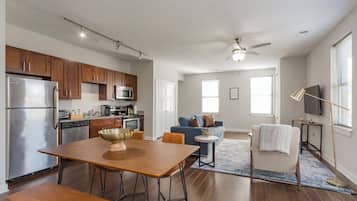 A modern kitchen with stainless steel appliances, a dining area with a wooden table, and a living room with a blue sofa.