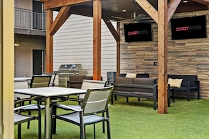 An outdoor patio area with a grill, seating, and a TV screen displaying 'COZY SUITES'.