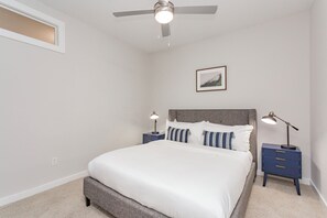Ein Schlafzimmer mit einem Bett, zwei Nachttischen mit Lampen, einem Deckenventilator, einem gerahmten Bild an der Wand und einem Fenster.