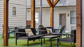 Un espacio al aire libre con sofás y sillones, una mesa y vistas a un edificio con balcón.