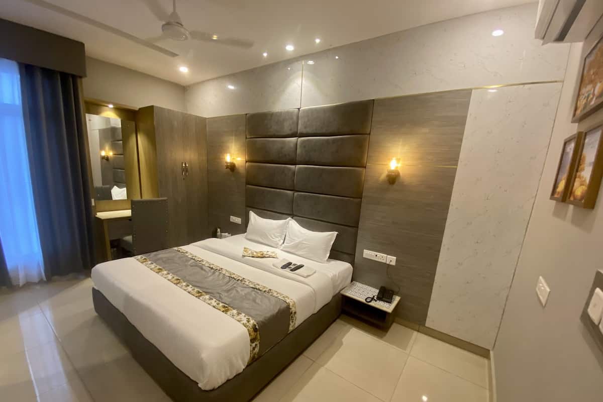 A modern hotel room with a large bed, a bedside table with a phone, and a wall-mounted light fixture.