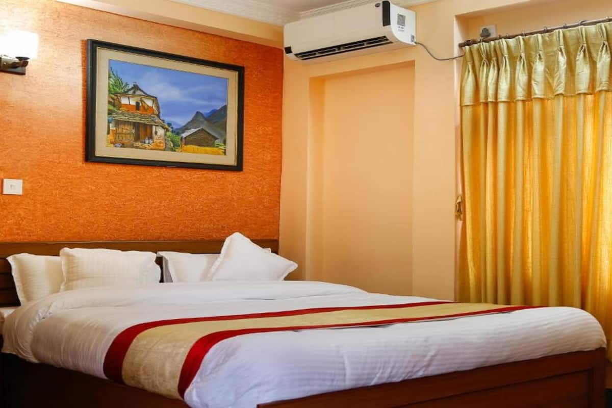 A hotel room with a bed, a painting on the wall, an air conditioner, and a curtain.