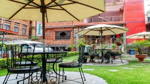 An outdoor seating area with tables and chairs, umbrellas, and a brick building in the background. - MeroStay 195  Hotel Garden  Pvt Ltd (Kathmandu)