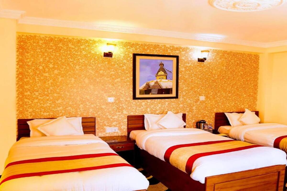 A hotel room with three single beds, each with a red and white bedspread. The room has a patterned wallpaper and a framed picture on the wall.