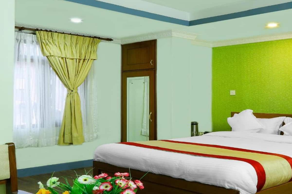 A hotel room with a bed, a window with curtains, a green accent wall, and a wooden door.