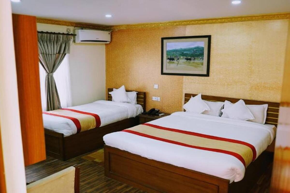 A hotel room with two beds, a wooden headboard, a mounted picture, and an air conditioning unit.