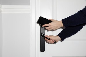 Una mano usando un teléfono inteligente para abrir una puerta.