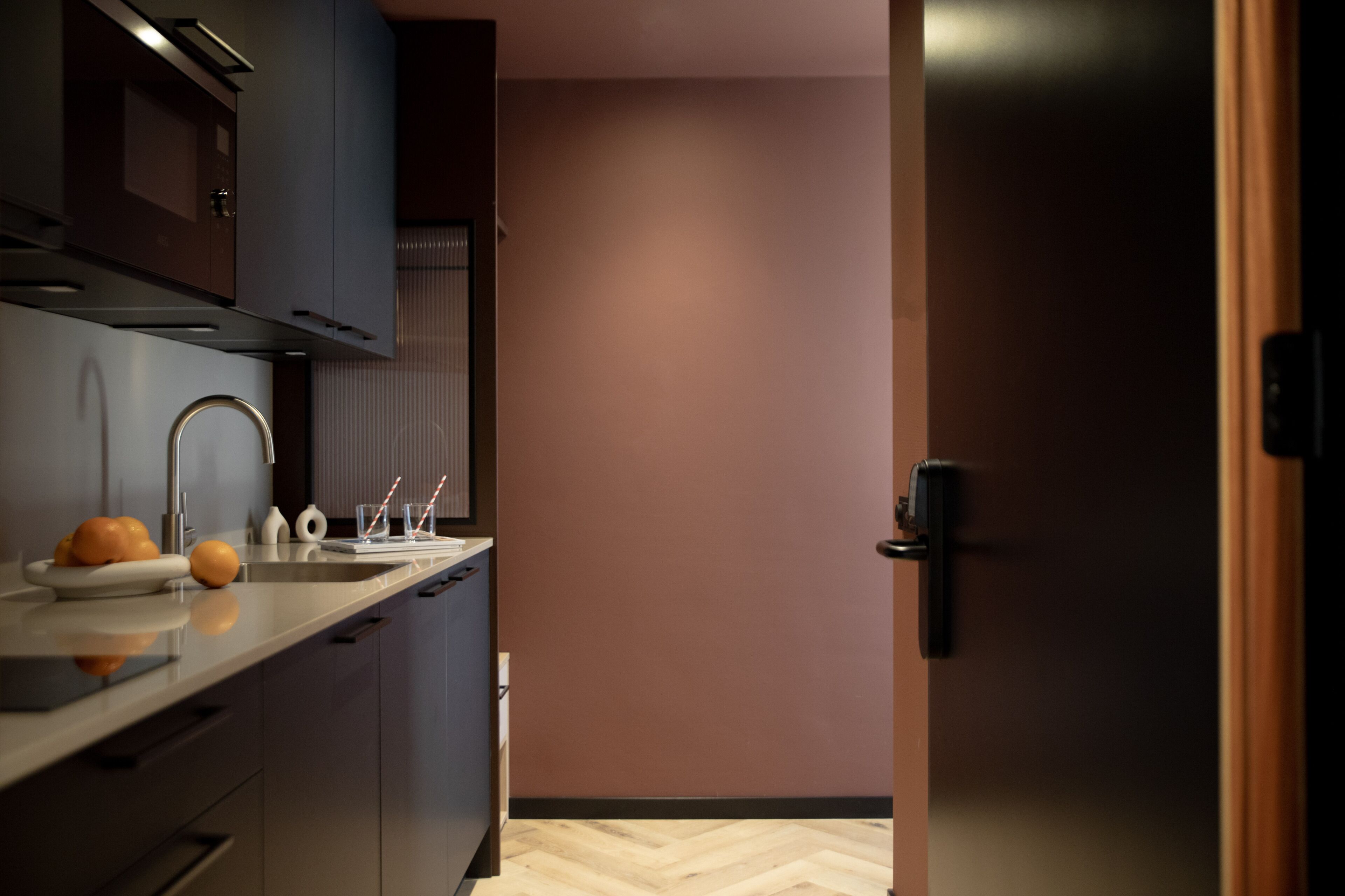A modern kitchen with a sink, cabinets, and a door leading to another room.