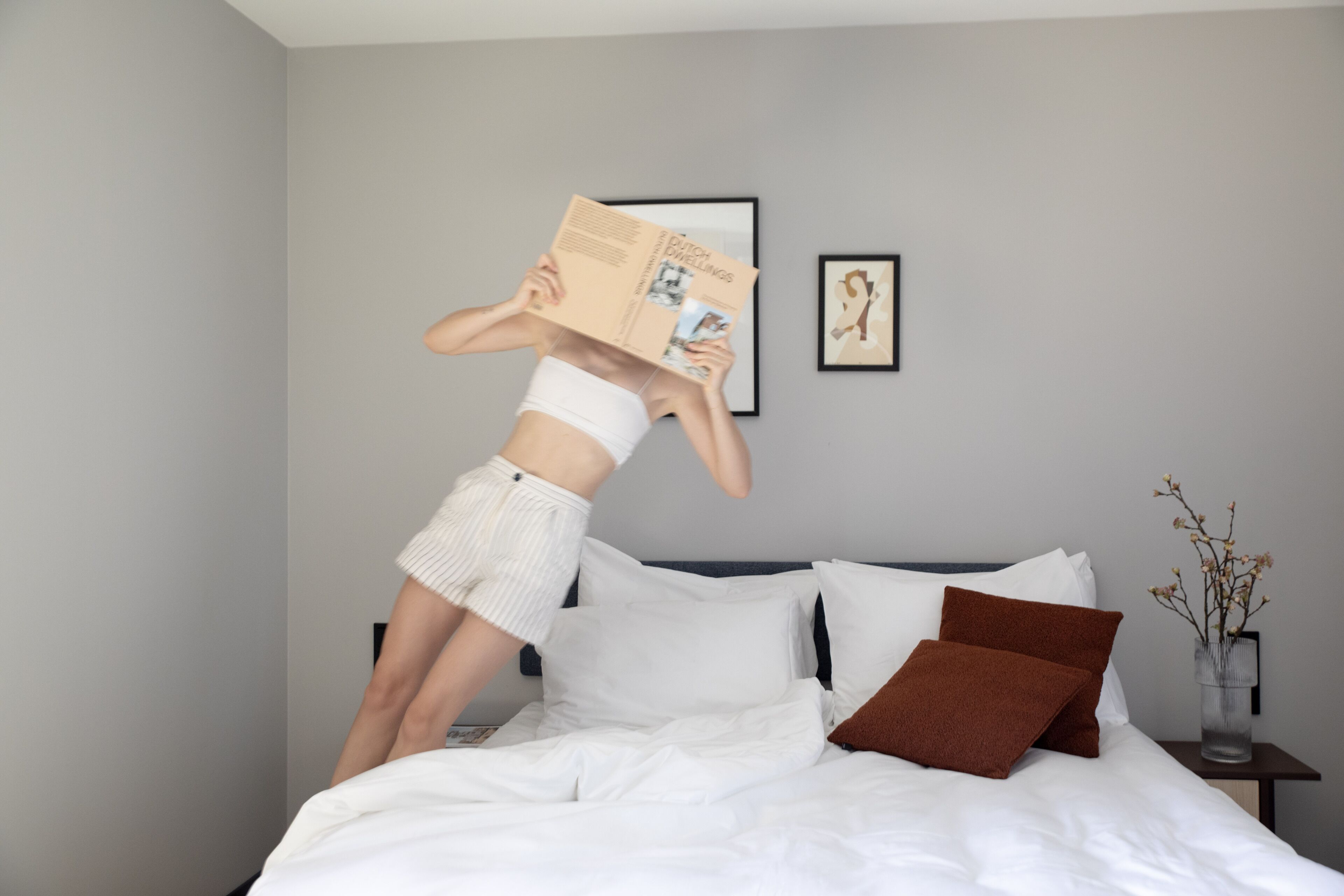 Un dormitorio con cama, almohadas, una mesita de noche y un cuadro en la pared.