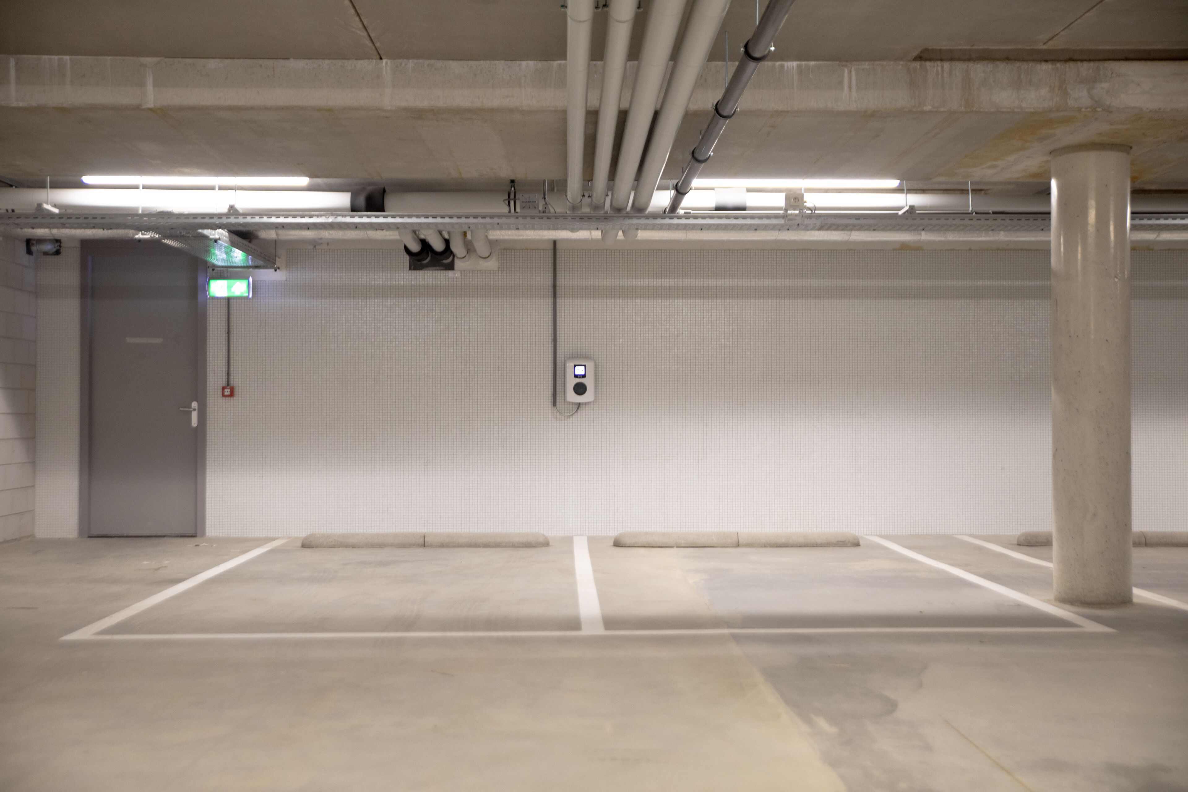 Un parking souterrain vide, avec des piliers en béton, une porte et un panneau de commande fixé au mur.