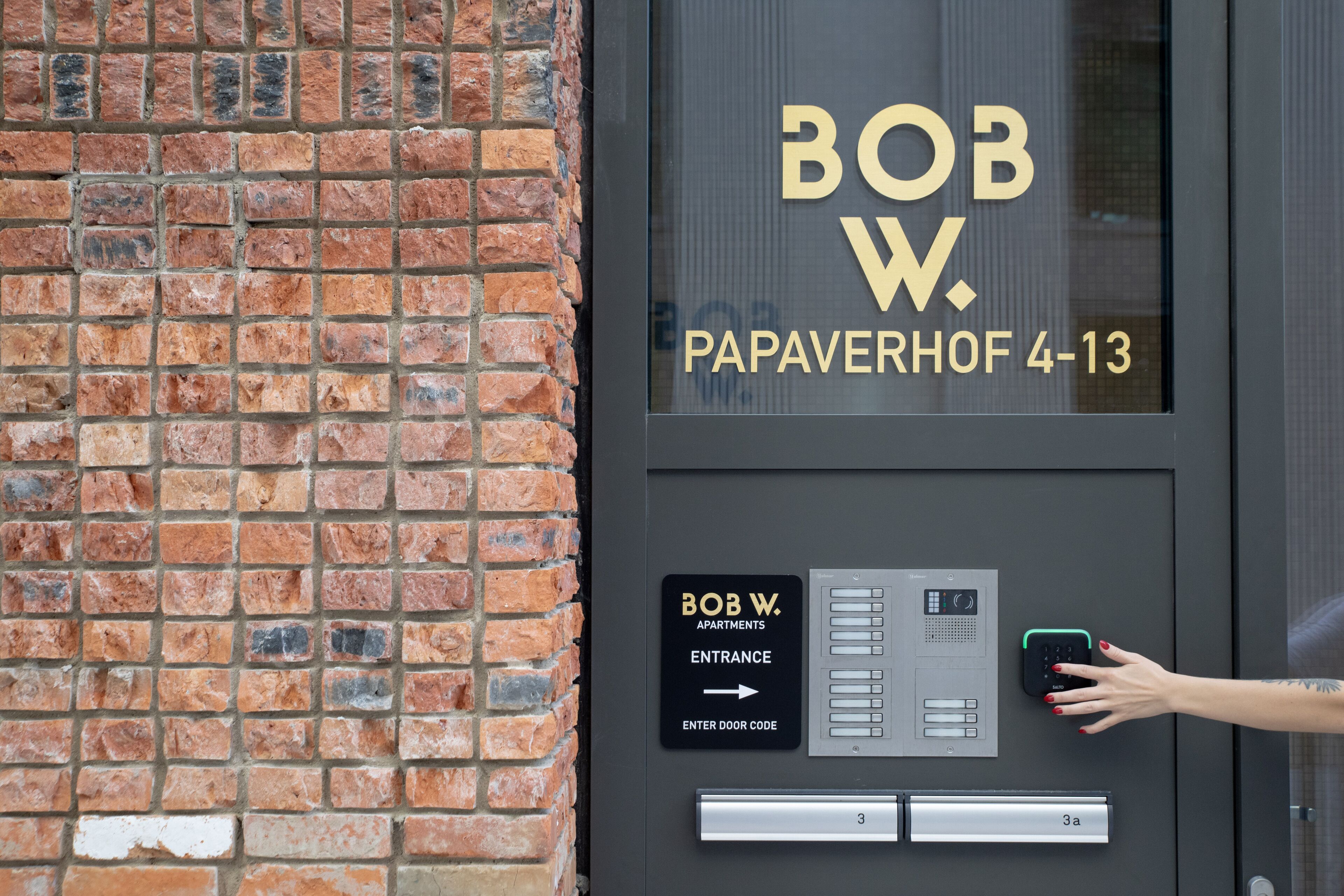 A hotel entrance with a brick wall, a sign for Bob W. Papaverhof 4-13, and a keypad for entering the door code.