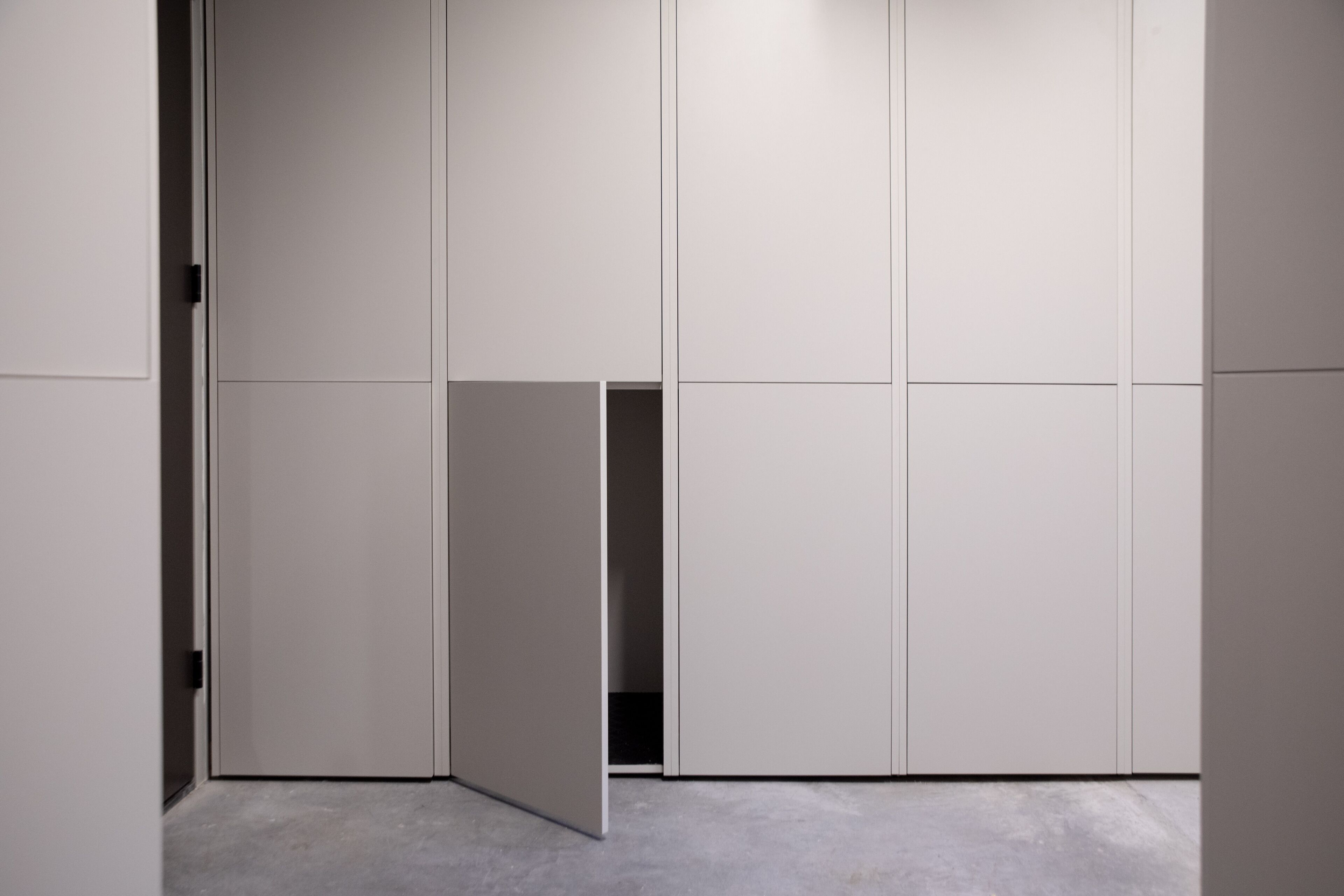 A modern, minimalist room with a large wardrobe, a small open closet, and a concrete floor.