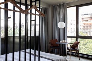 Habitación de hotel con cama, dos sillas, una mesita y una lámpara colgante.
