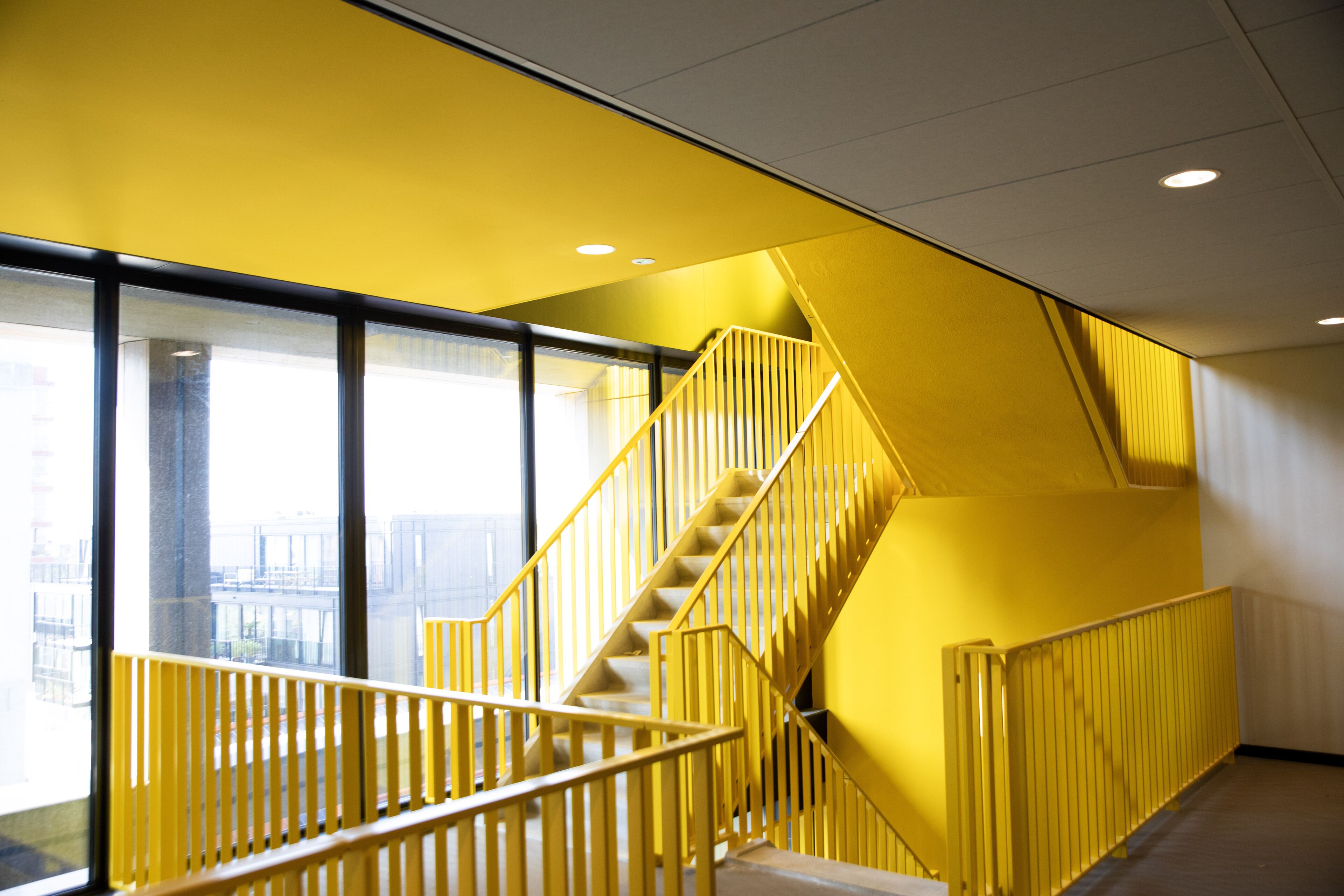 Eine Treppe mit gelb lackierten Geländern in einem Gebäude mit großen Fenstern.