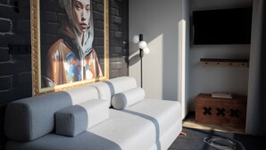 A modern living room with a grey sofa, a framed painting, a black floor lamp, a wooden chest, and a mounted TV. - Bob W Amsterdam Noord (Amsterdam)