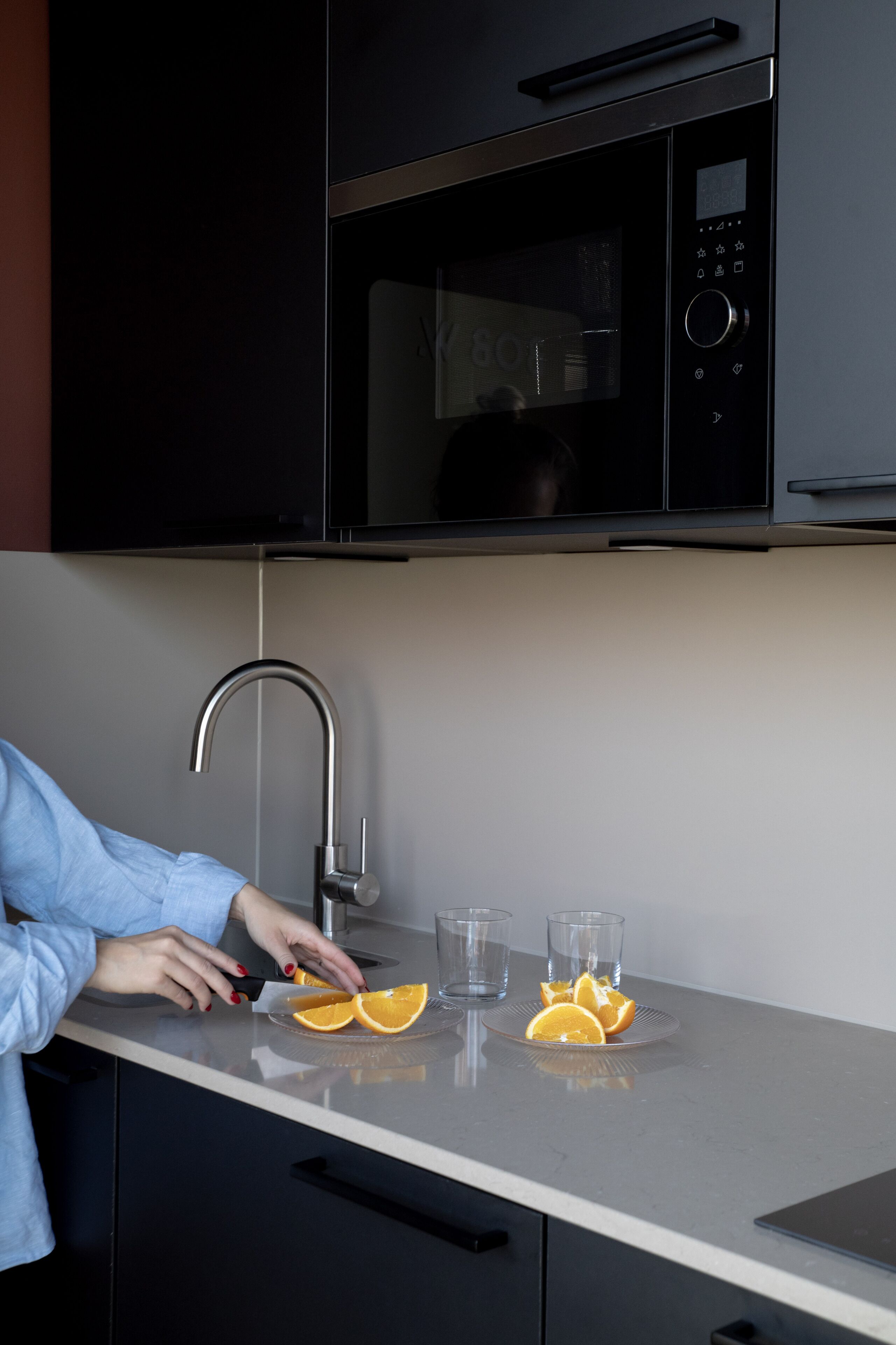 A kitchen with a microwave, a sink, and a countertop with sliced oranges and glasses.